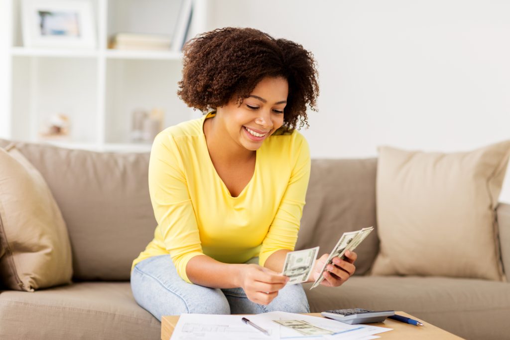 A-woman-sitting-on-her-couch-budgeting-and-counting-money-Ground-Picture-Shutterstock