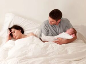 Father taking care of baby while mother tries to rest (postpartum depression)