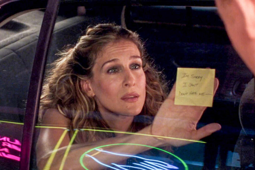 An image of Carrie Bradshaw holding a Post-in note in "Sex and City" as part of a story on how to navigate a breakup during cuffing season.