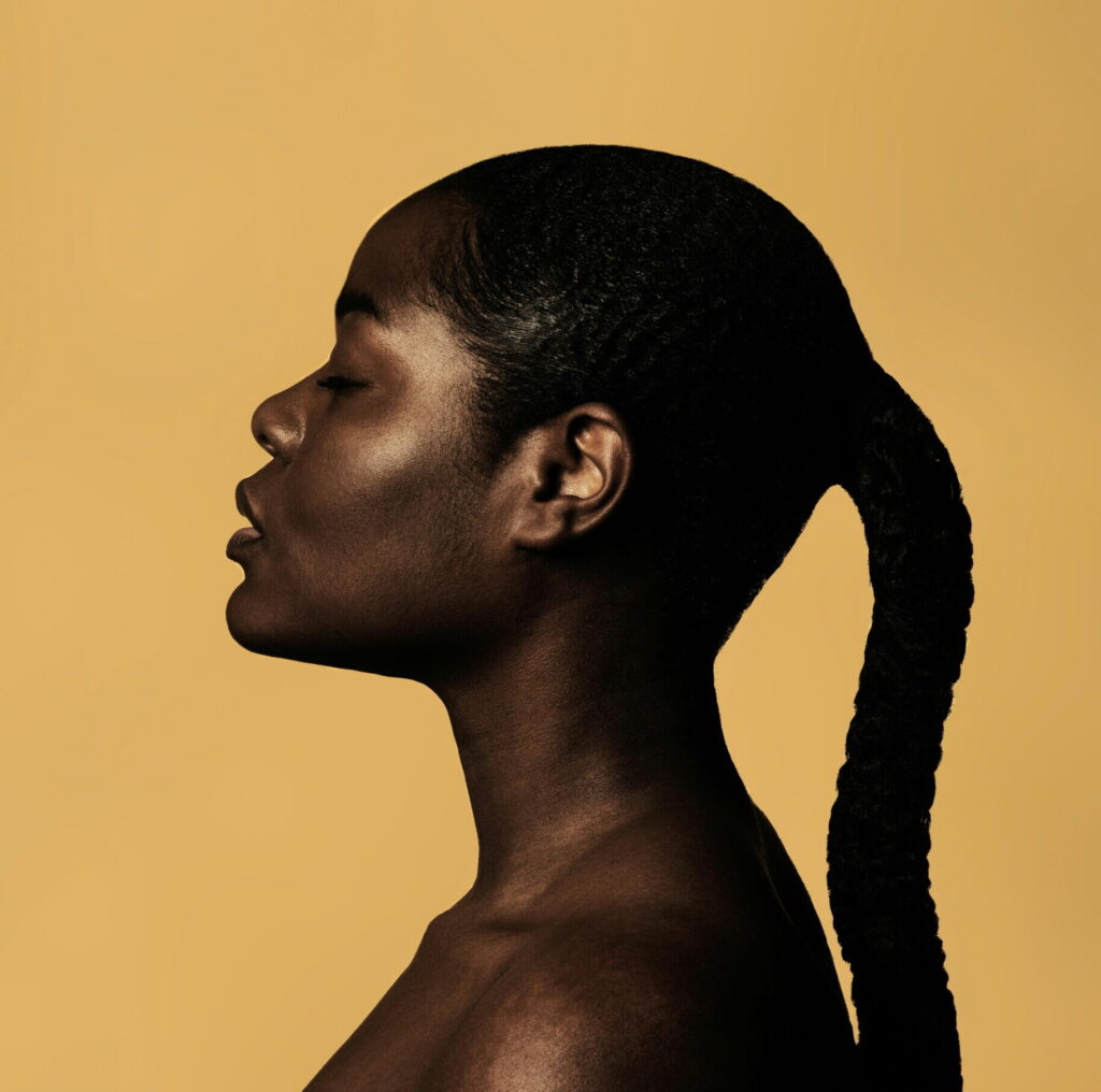 Side profile of a Black woman against a yellow background as part of a story on stepping into your feminine energy. (Credit: Jessica Felicio via Unsplash)