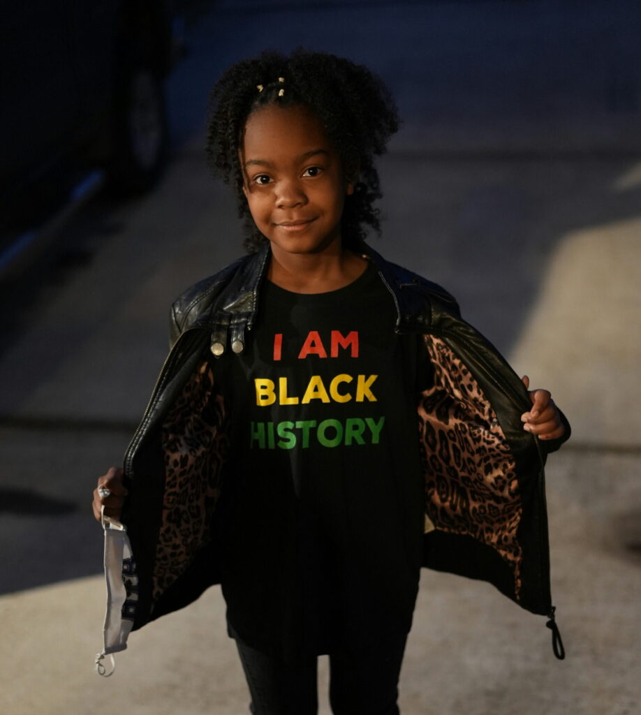 Young Black girl wearing a "I Am Black History" t-shirt as part of a story on ways to teach your kids history when the truth is being erased. (Credit: Anthony McKissic via Unsplash)